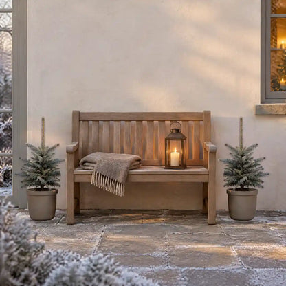 Zwei Blaufichten in greigen Kübeln neben einer Holzbank auf der Terrasse im Winter