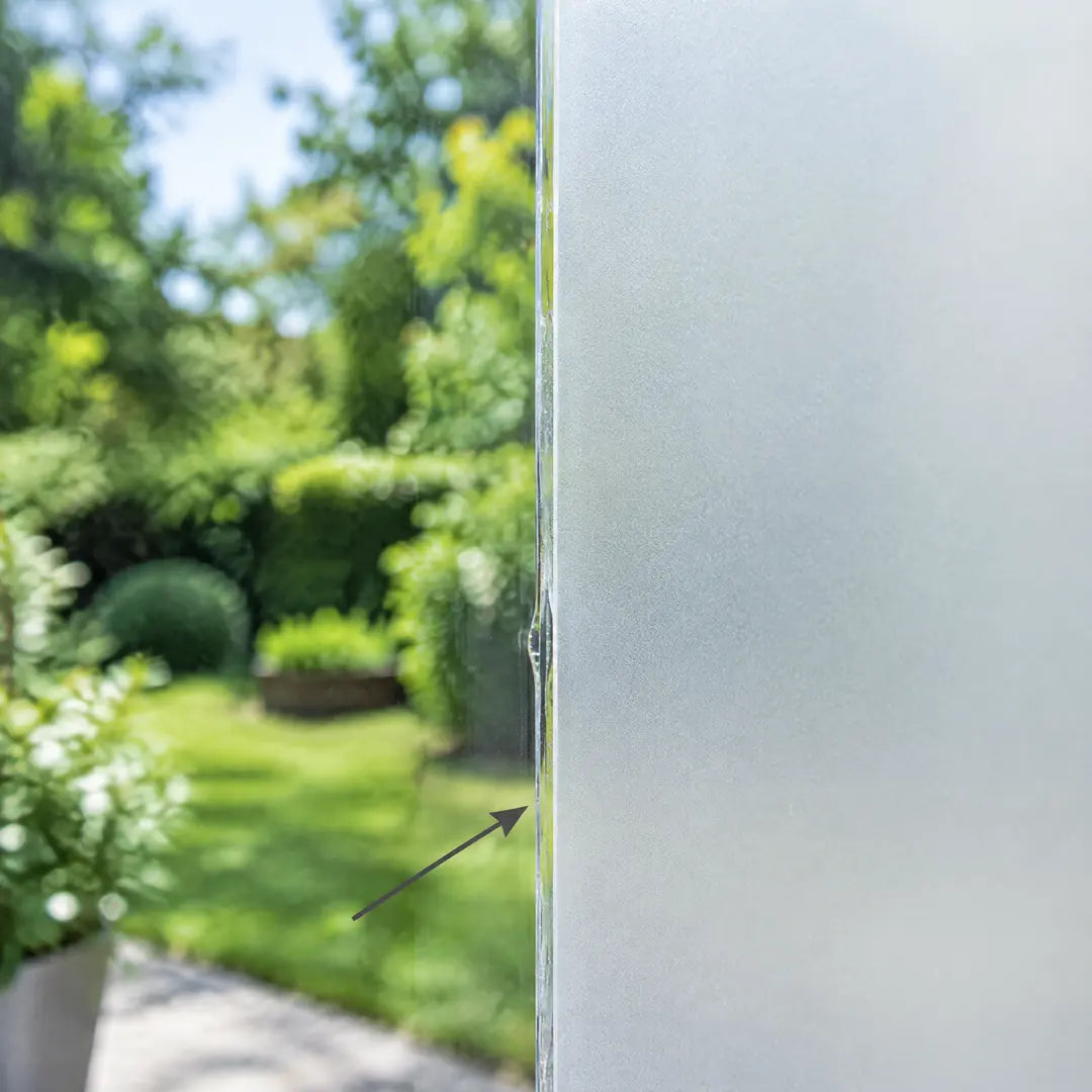 Fensterscheibe halb mit Sichtschutzfolie beklebt, daneben freier Blick in den Garten