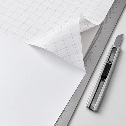 Schutzpapier mit Zentimeter-Raster, daneben Cutter und Lineal