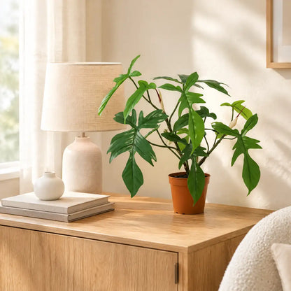Künstlicher Philodendron Florida auf einem Eichen-Sideboard neben einer Tischlampe im hellen Wohnzimmer