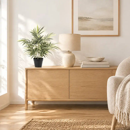Künstlicher Bambus auf einem hellen Sideboard im Wohnzimmer neben Tischlampe und Büchern