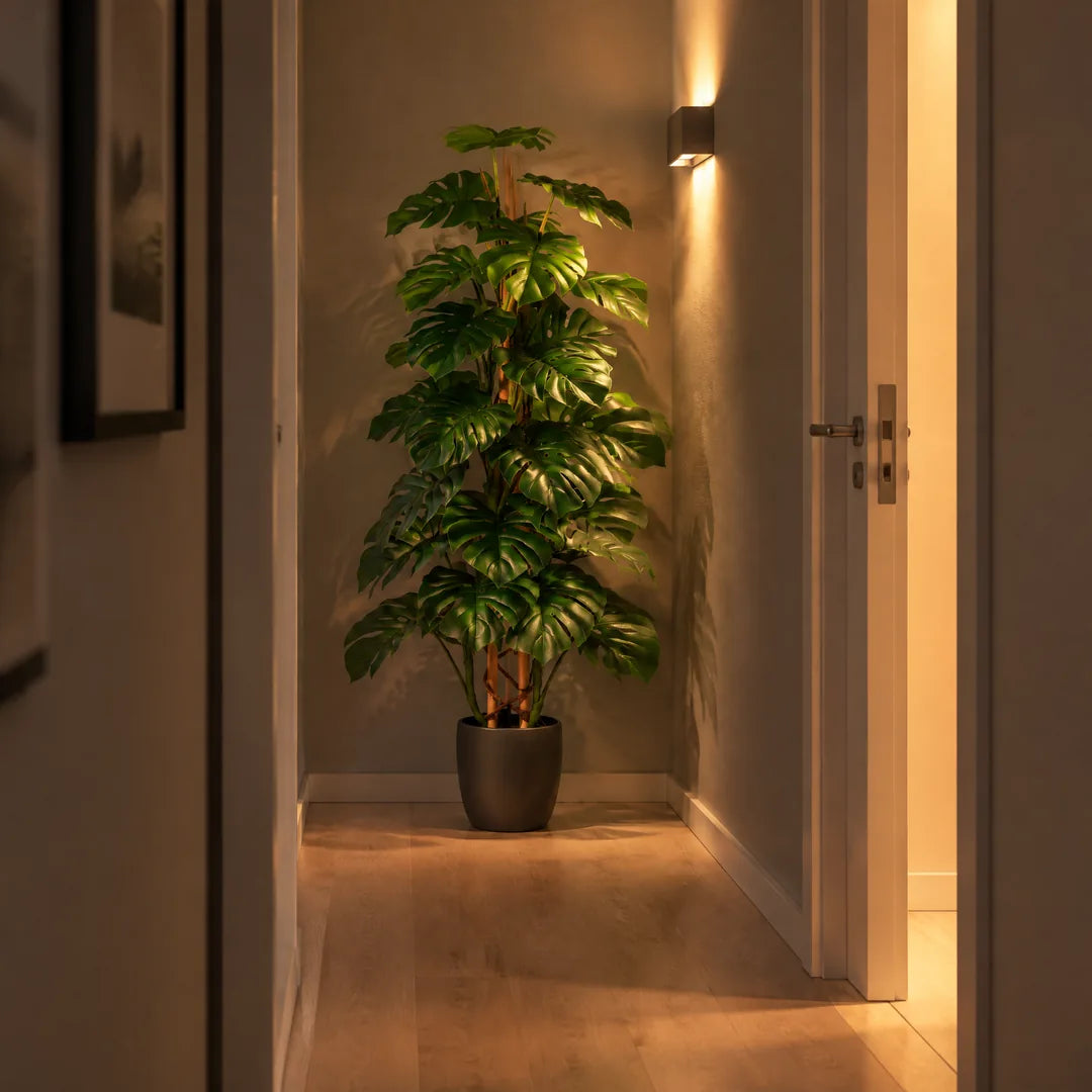 Künstliche Monstera im fensterlosen Flur, beleuchtet von einer Wandleuchte