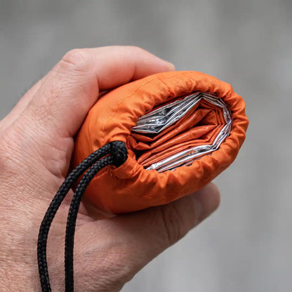 Hand hält den zusammengefalteten Notfallschlafsack im Packsack, handtellergroßes Packmaß