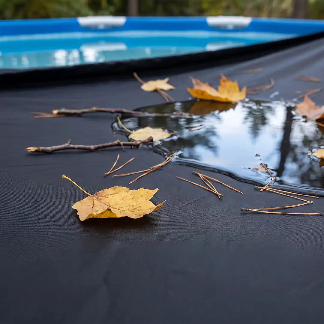 Nahaufnahme: Herbstlaub und Zweige liegen auf der Poolabdeckung statt im Wasser
